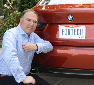 Man poses with his car's rear tags that say "Fintech"